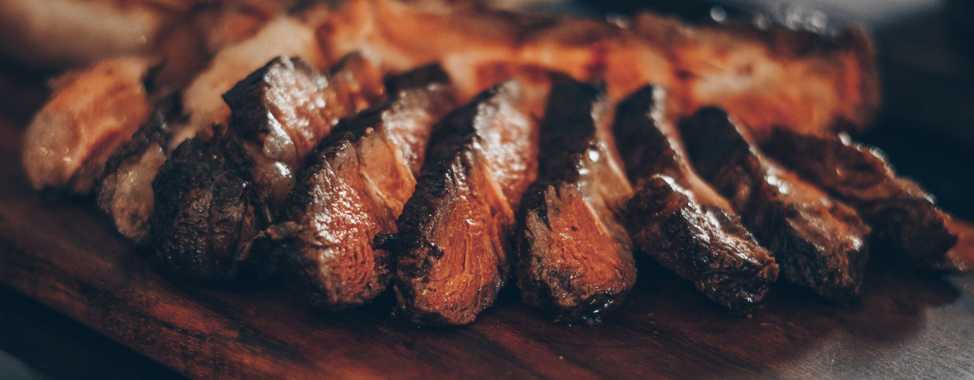 Close-up of sliced grilled beef brisket on a wooden board, showing juicy bark and smoke ring