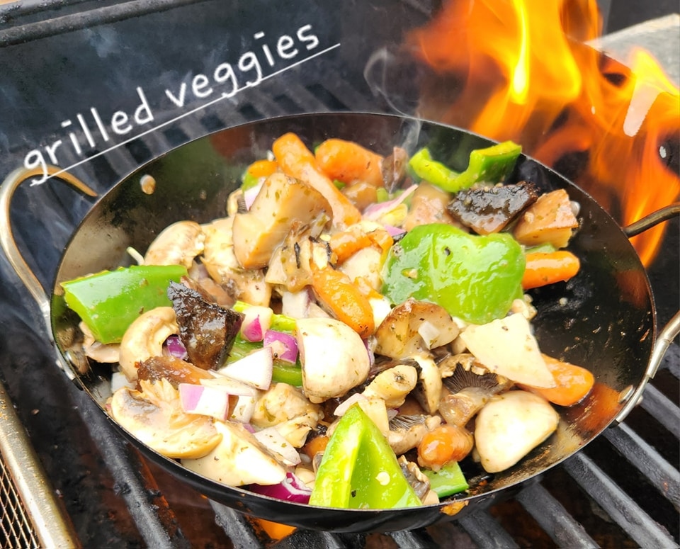 Cast-iron wok of grilled veggies—peppers, mushrooms, onions—over open flame on the Van’s Grill BBQ, with ‘grilled veggies’ text on the image.